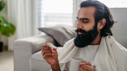 Man holding a mug of tea and a temperature gauge.