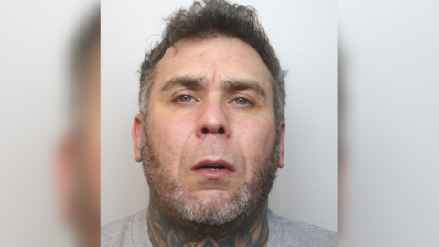 A mugshot of Dean Snarey, who has a short, grey beard and a tattooed neck.