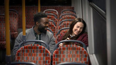 Paapa Essiedu and Siobhán Cullen sitting on the bus and laughing 