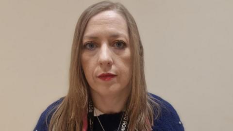 Dr Clodagh Corrigan looks into the camera. She has shoulder length brown hair, blue eyes and is wearing red lipstick. She is wearing a navy jumper.