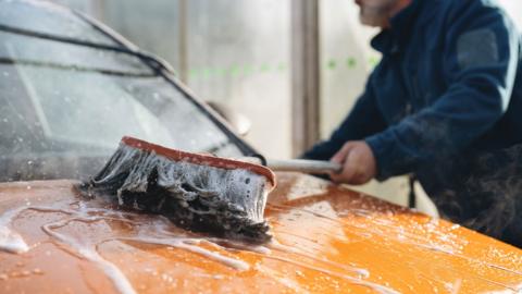 Driver actively cleaning orange car using foam brush and soapy water
