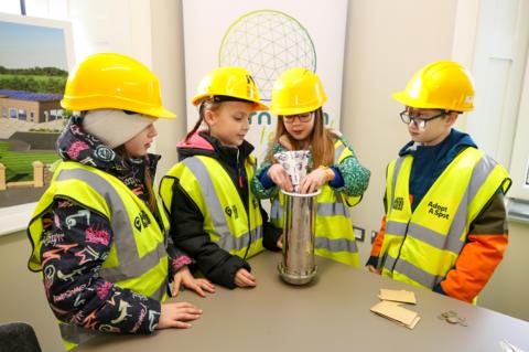 four children in high viz jackets place items in a time capsule