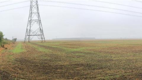 Site of the solar farm an open field with an electricity pylon in one corner