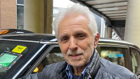 A man stands in front of a black cab