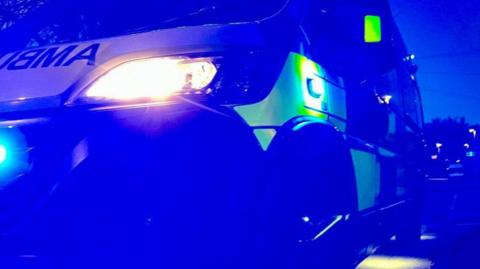 A close up image showing an illuminated ambulance in blue light that is pictured on a residential street. 