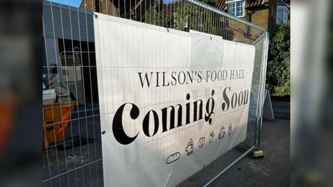 A white sign displayed on a fence advertising Wilson's Food Hall