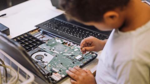A stock image of a boy using a small screwdriver on what appears to be a laptop computer.