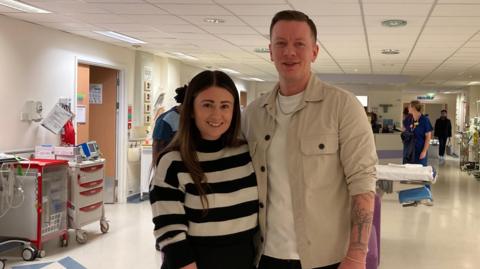 A man and woman stand smiling in a hospital ward
