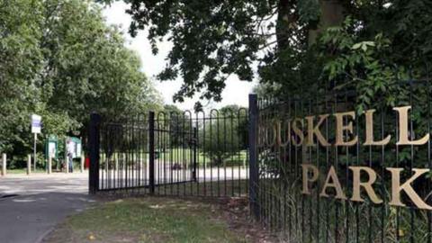 The sign for Bouskell Park on a black railed fence.