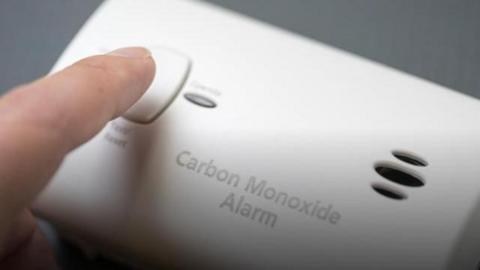 A finger pressing a button on a white carbon monoxide alarm. 