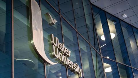 A row of windows with Ulster University written across them in silver. 