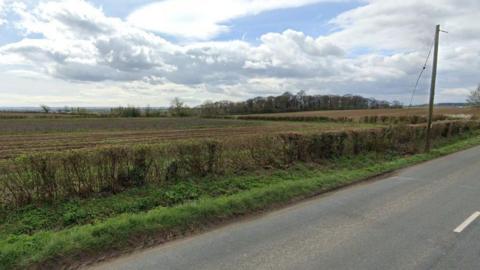A large open field beside a road, separated with a trimmed hedge. 