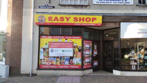 The exterior of Easy Shop, which is red and yellow, with an enforcement poster on the front window.