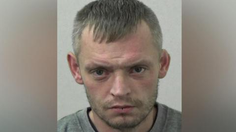 Mugshot of Michael Curran. He has short white hair and a faint grey beard.