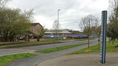 Single carriageway road outside school. Sign for Stockbridge Village in the foreground.