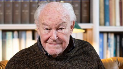 Timothy West pictured with a book shelf behind him