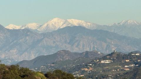 a snow capped mountain is seen looming above the green Santa Monica Mountains in Los Angeles 