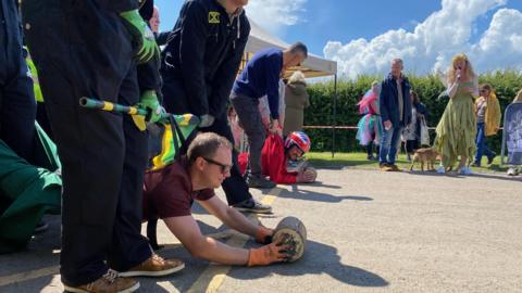 Men preparing to roll Stilton cheese on concrete, watched by onlookers