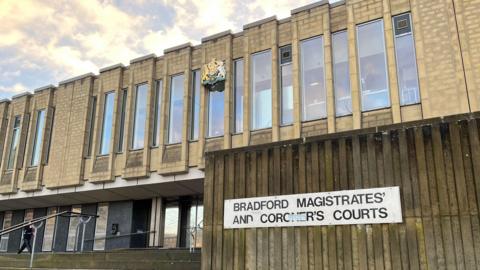 The entrance of Bradford Magistrates' Court, with steps leading up to the front doors. The building has several vertical windows, with a white sign in the foreground reading: "Bradford Magistrates' and Coroner's Courts."