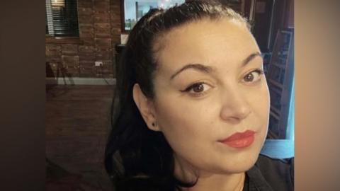 A headshot of Tina Ion. She has long brown hair and is wearing red lipstick.