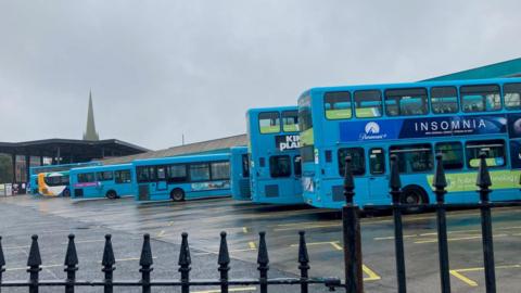 A large bus station with a number of blue double and single decker buses parked up
