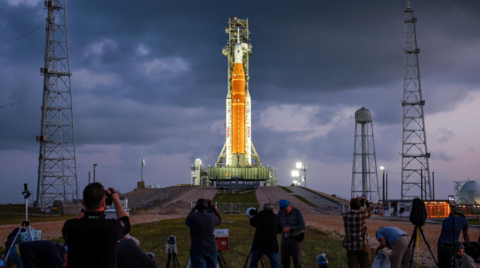 People set cameras to photograph NASA's Artemis II lunar flyby mission in front of a dark cloudy sky