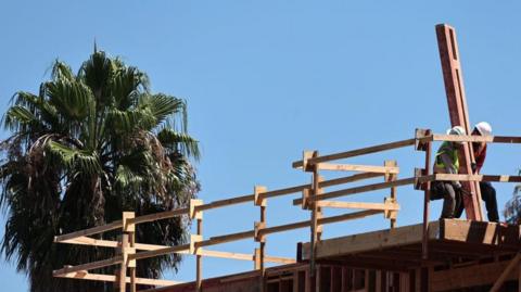 Construction worker holds a beam as he builds a mixed-use apartment complex on August 20, 2024 in Los Angeles, California. 