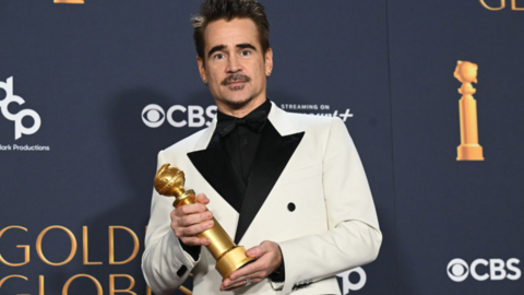 Colin Farrell holding golden globe award in white suit jacket