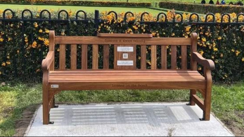 A bench placed on a concrete slab. It is placed in front of a metal fence.
