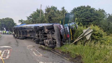An overturned lorry that has come off the road and landed on its side 