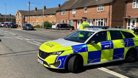 A police officer standing next to a police car in the road in the Farley Hill area of Luton