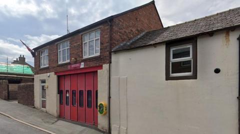 Lazonby on-call station is a small two-storey building with a red shutter door.