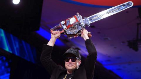 Elon Musk holds a chainsaw. 