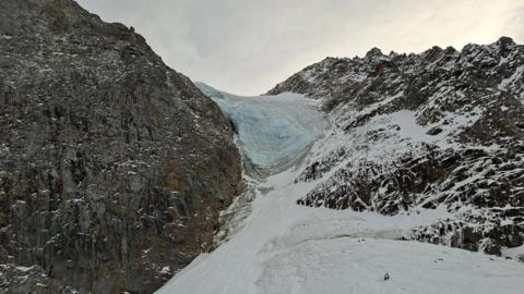 A rocky mountain is seen covered in snow and a glacier 
