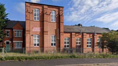 A Google Street view of the red-bricked property from the road. It is long and has several sets of windows. Half of the building has two-storeys, the other has one.