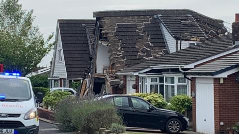 Tiles slide down collapsing roof of house with cars in drive outside