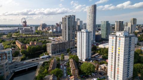 An aerial view of high-rise tower blocks and new apartment buildings in Stratford, with roads, waterways and the Olympic Park visible in the distance.