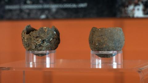 Close up views of two Bronze Age pinch pots displayed in an exhibition case against an orange background at Peterborough Museum