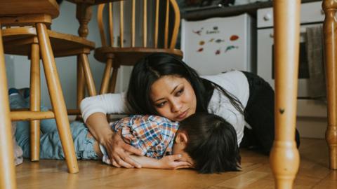 Woman holds onto child under a table