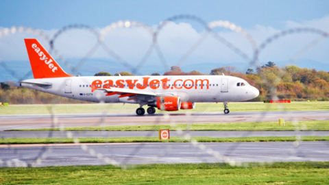 An EasyJet plane on the runaway at Manchester Airport, seen through barbed wire on top of a fence