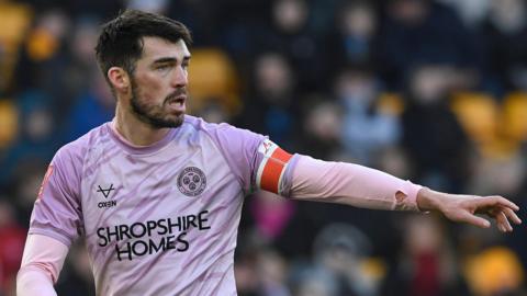 John Marquis in his pink away kit directs his team-mates during a game for Shrewsbury