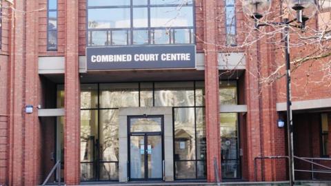 A red brick building with a see-through glass entrance and an automatic door at the front. Above the door it says "Combined Court Centre".