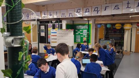 Children in a classroom with metal poles and beams to hold the ceiling up