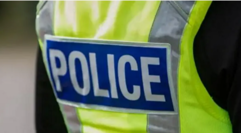 The back of a police officer's hi-vis jacket. It it florescent yellow and has the word police in white capital letters on a blue background on it. 