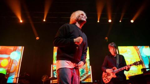 Tim Burgess of The Charlatans performing at the O2 Academy in Leeds in 2023. He has mopped blonde hair and is wearing a dark-coloured top. 