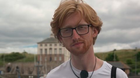 Patrick Safford at Eyemouth harbour, he has red hair, wears glasses and a white t-shirt with Berwickshire Marine Reserve on it