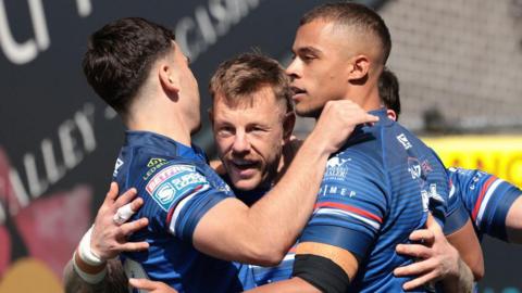 Tom Johnstone is surrounded by team-mates, all in Wakefield Trinity blue, as they celebrate one of his three tries against Bradford Bulls.