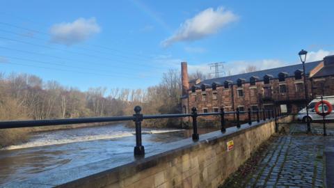 A historic red brick mill with a river in front of it.
