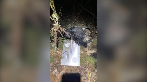 A hole with a spade beside it and a piece of burnt out signalling equipment.
