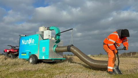 A machine which is used to clean microplastics off a beach. It looks like a giant hoover and is bright blue. 